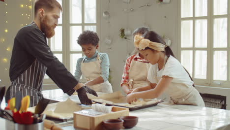 Niños-Y-Chef-Poniendo-Masa-En-Bandejas-Para-Hornear-Durante-La-Clase-De-Cocina